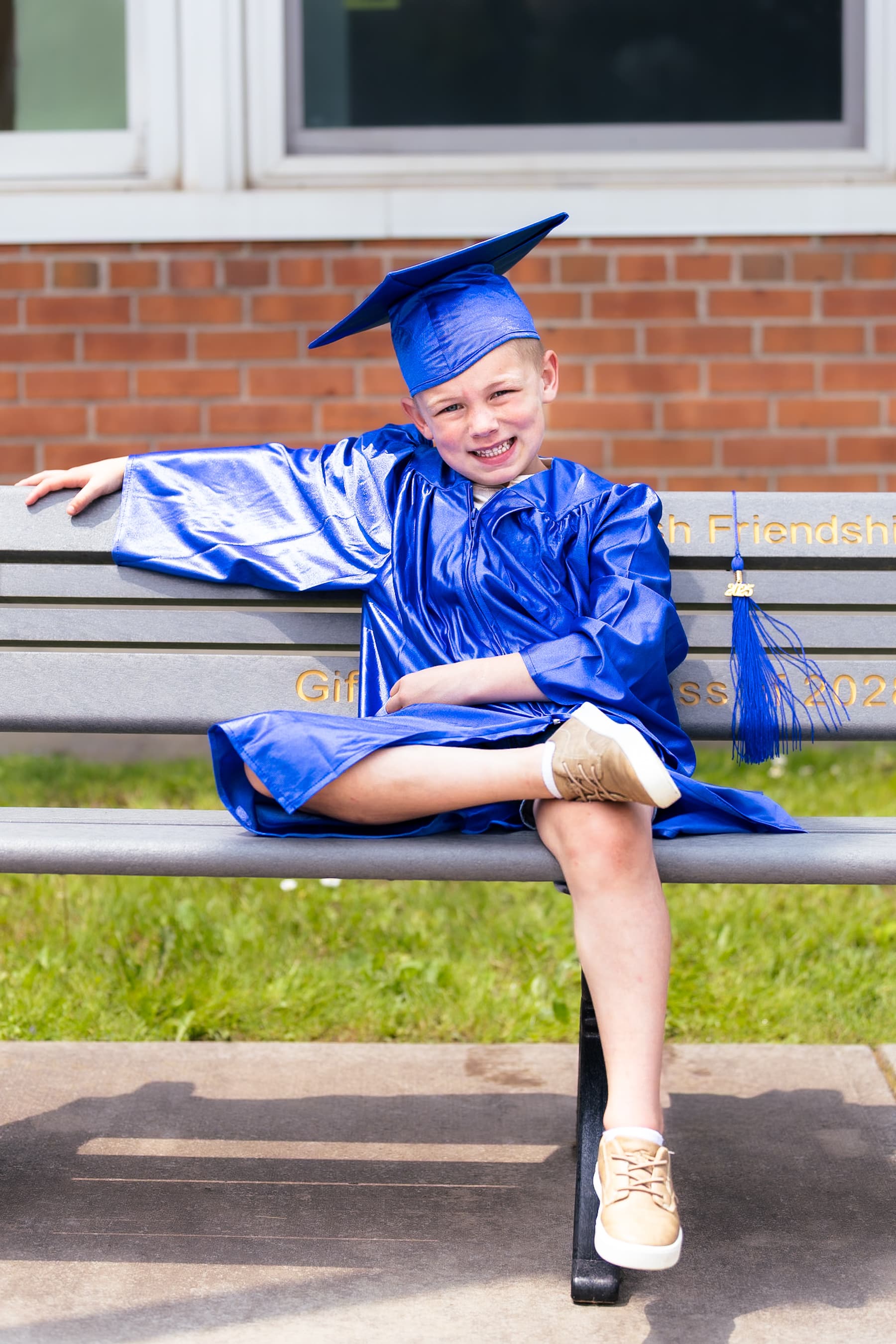 Young boy in blue graduation cap sitting on bench