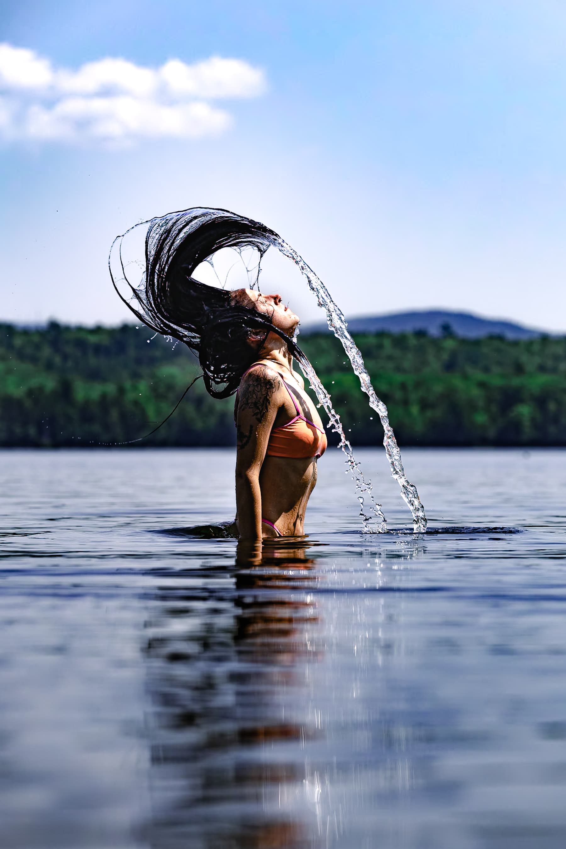 Woman flipping hair in lake creating water arc
