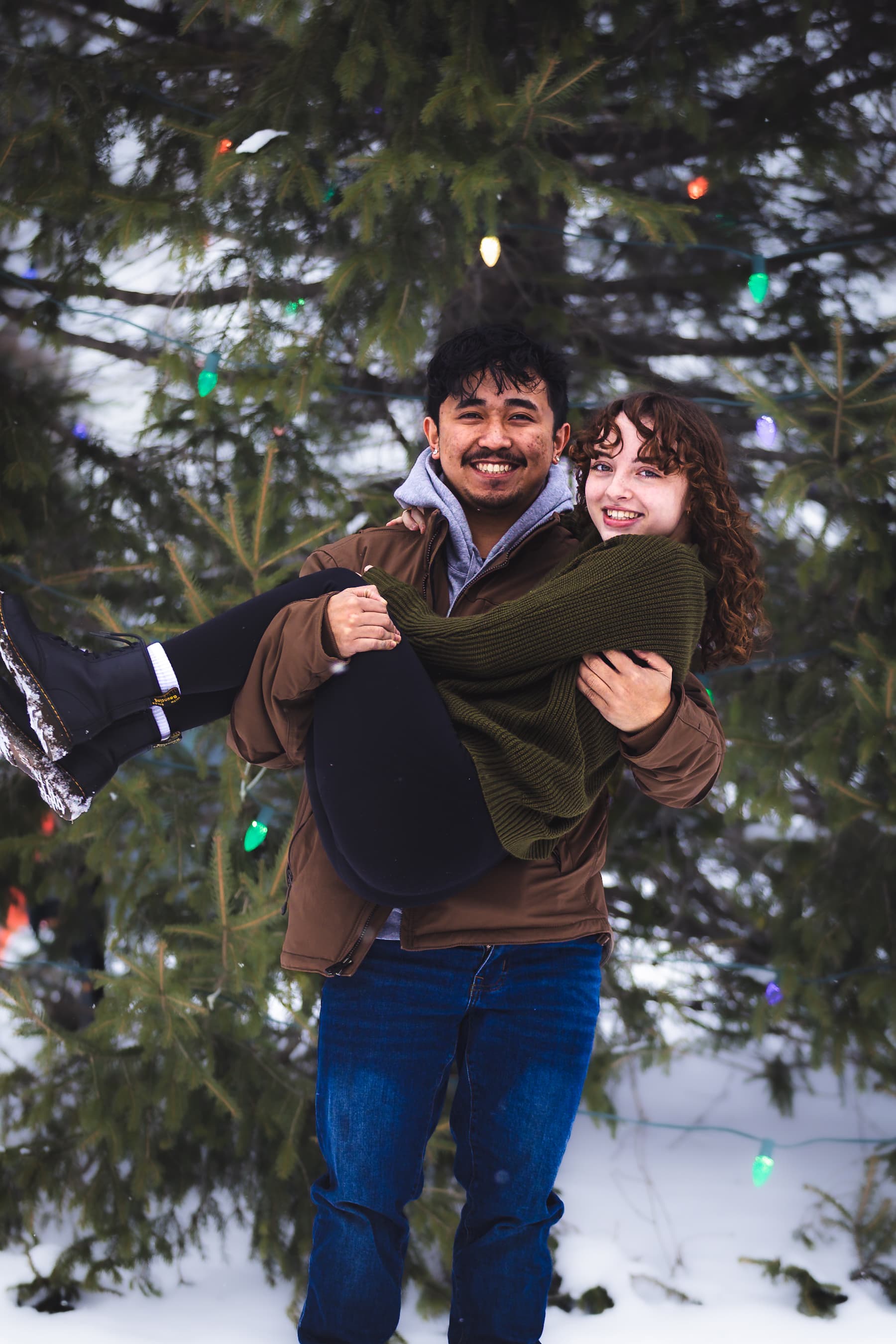 Couple laughing in snow with Christmas lights