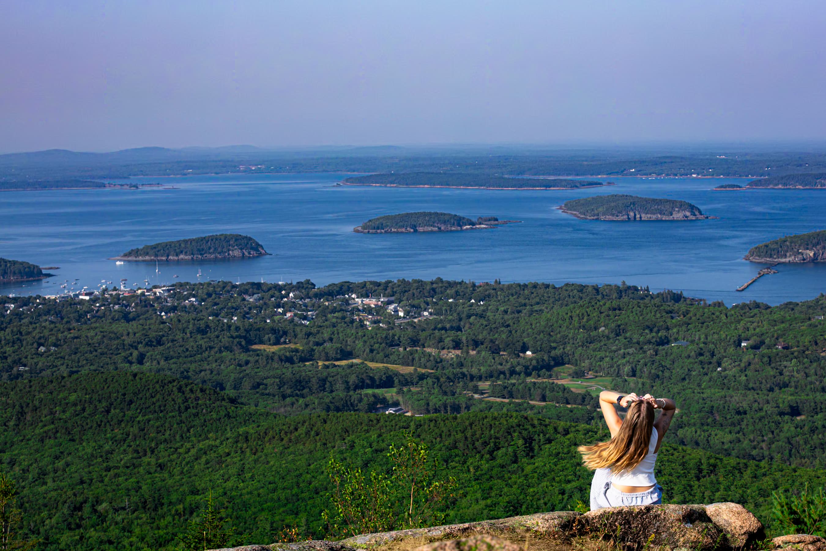 Woman sitting on a cliff edge looking out over a bay of islands